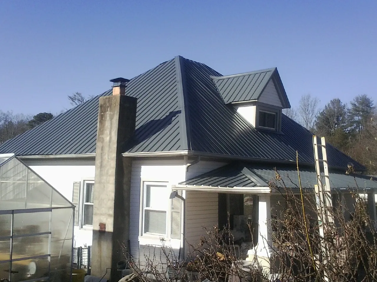 Dark blue standing seam metal roof on a white farmhouse with dormer — Slate & Tile Roof Repair by Roofing Brothers in Iselin