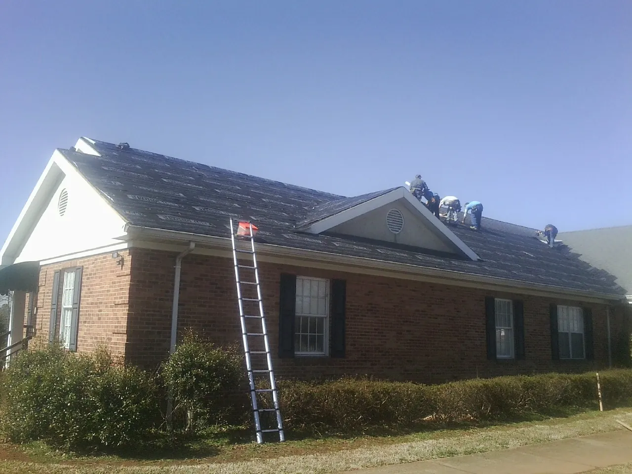 Crew tearing shingles off a brick ranch roof with a ladder set — Metal Roof Repair work by our crew in Iselin