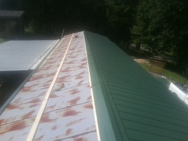 Old rusted panels beside newly installed green metal roofing — Wind Damage Roof Repair by Roofing Brothers in Iselin