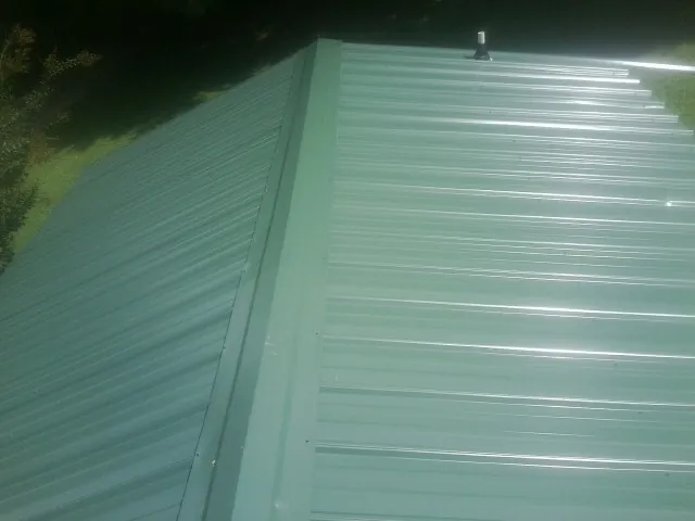 New green metal panels meeting at the ridge of a roof — Flat Roof Repair work by our crew in Iselin
