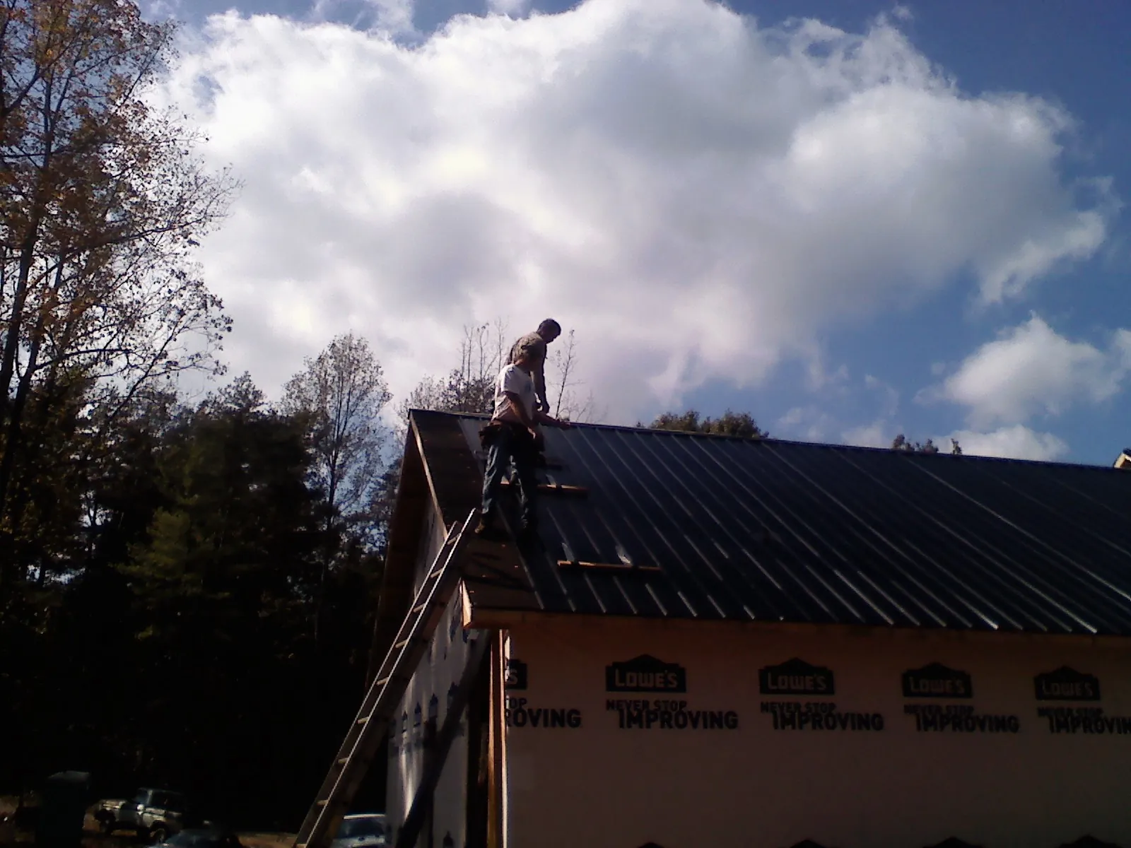 Roofer fastening dark metal panels high against a cloudy sky, from a Roof Inspection job in Iselin